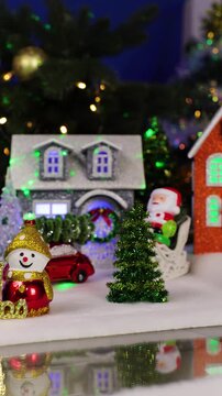 In the foreground of a large Christmas town are two snowmen with letters and an unusual Santa Claus jumps out