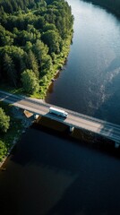 Obraz premium Truck drives across bridge over dark river. Green forest surrounds water. Aerial view shows isolated road and nature. Summer sun casts long shadows.