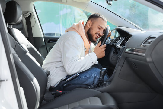 Handsome young man hugging steering wheel in car. I love my car concept
