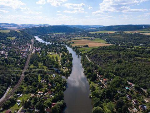 A breathtaking aerial view of a winding river flowing through a lush green valley, surrounded by rolling hills, scattered villages, and patchwork fields beneath a bright summer sky.
