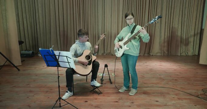 Boy and Girl Practice Playing Music on Stage. Kids Play Guitar and Bass Guitar. 4K 10-bit