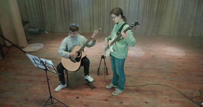 Boy and Girl Practice Playing Music on Stage. Kids Play Guitar and Bass Guitar. 4K 10-bit