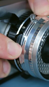 Extreme close up of a professional photographer fingers manually adjusting the metallic aperture ring on a classic analog camera lens to set correct exposure before taking picture. Vertical video.