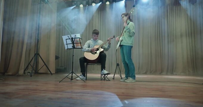 Boy and Girl Practice Playing Music on Stage. Kids Play Guitar and Bass Guitar. 4K 10-bit