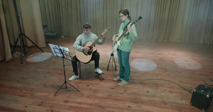 Boy and Girl Practice Playing Music on Stage. Kids Play Guitar and Bass Guitar. 4K 10-bit