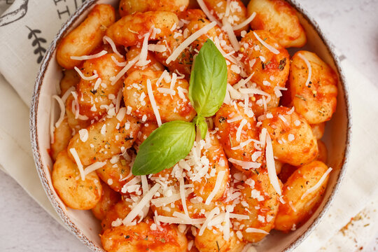Bowl of tasty gnocchi with cheese on white background