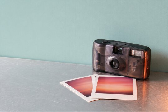 Disposable camera with two developed photographs on a metallic table. Retro photography equipment for film capturing. Analog nostalgia concept, vintage hobby and capture memories.