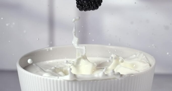 Different berries falling into a bowl of milk with splash in super slow motion