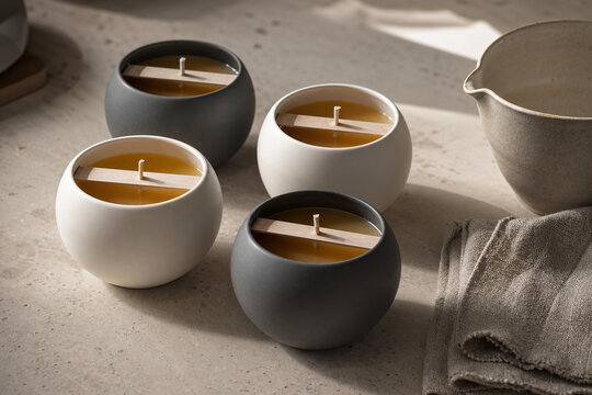 Four round ceramic candles with wooden wicks arranged on a neutral stone surface, styled with soft linen and warm sunlight.