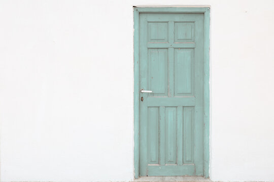 Caption: A mint green wooden door set in a white wall in Plaka, Milos, Greece, showcasing traditional Cycladic architecture and minimalist design.