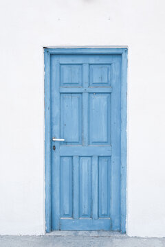 A light blue wooden door framed by a white wall in Plaka, Milos, Greece, capturing the simplicity of Cycladic design.