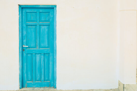 A bright turquoise wooden door contrasts against a white wall in Plaka, Milos, Greece, reflecting colorful Cycladic charm.