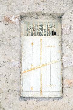 A weathered window with rusted metal bars set in a stone wall in Plaka, Milos, Greece.