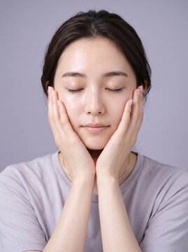 Young Japanese woman cupping her face against a soft neutral background, beauty and wellness concept, suited for dermatology and healthcare content