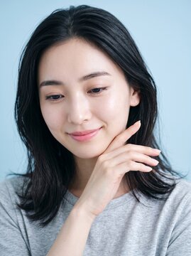 Young Japanese woman with a shy smile in a bright indoor studio setting, natural beauty and skincare concept, great for wellness and self care marketing