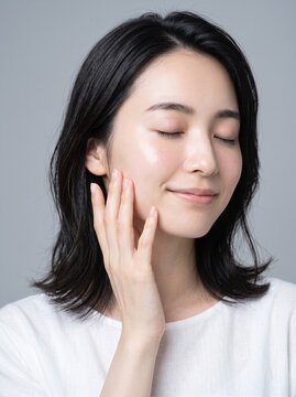 Young Japanese woman touching her cheek in natural daylight at home, skincare routine and self care concept, well suited for lifestyle and beauty blogs