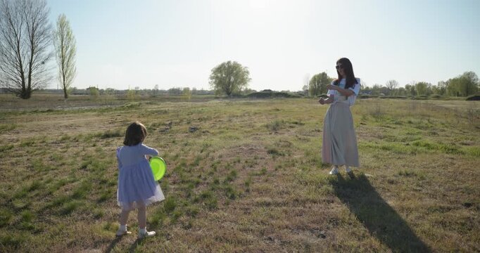 Mother with Children Throw Flying Disk Playing Outside. Family spend time together on nature. 4K 10-bit