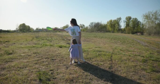 Mother with Children Throw Flying Disk Playing Outside. Family spend time together on nature. 4K 10-bit