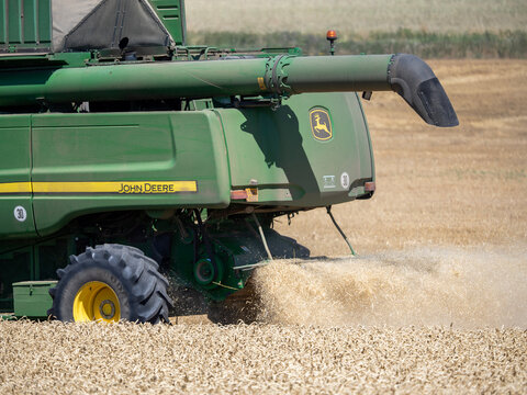 Louny, Czech Republic - July 25, 2026: Close-up of a John Deere combine harvesting ripe wheat as straw, chaff and dust pour from the rear.