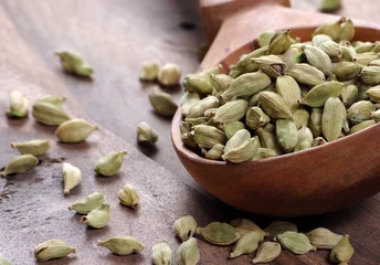 green cardamom pods in a wooden spoon on a wooden table. close up © Oleksii