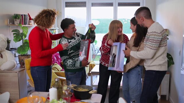 Happy multi generational family wearing festive sweaters exchanging presents and opening a bottle of champagne, celebrating christmas together in a cozy, decorated living room with a dinner table
