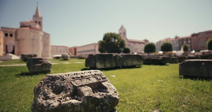 Close view of an ancient Roman stone fragment at the Roman Forum archaeological site with the Church of St Donatus in the background.