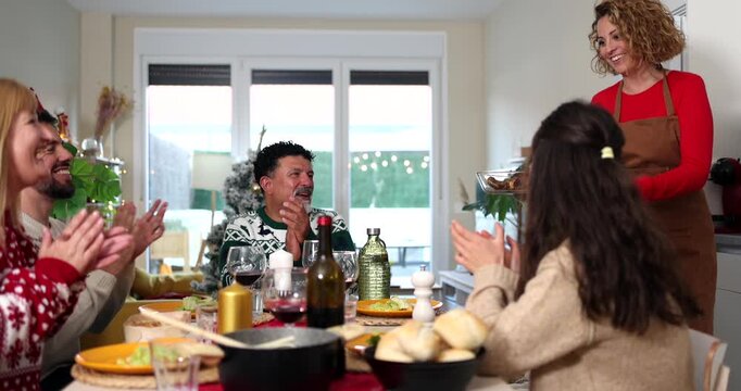 Happy multi generational family clapping as a woman serves the main course at a christmas dinner table, enjoying a festive gathering and celebrating the holiday season together at home