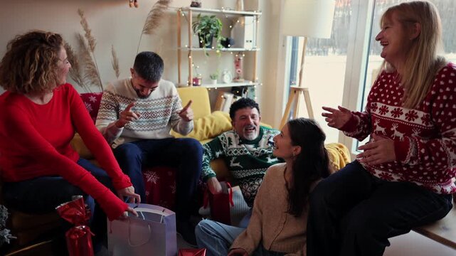 Happy family gathering in a cozy living room, laughing and clapping hands while exchanging presents during christmas holidays, celebrating together with joy and wearing festive sweaters