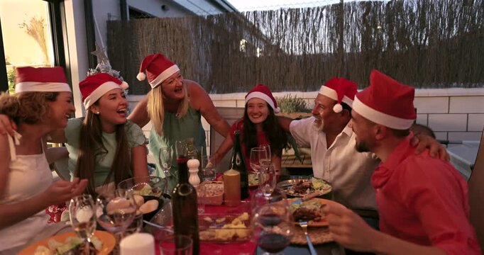 Joyful multi generational family, laughing, and clapping during a festive christmas dinner party outdoors, creating cherished holiday memories together