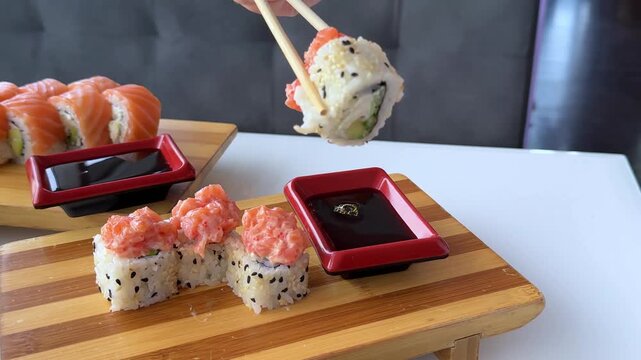 A specialty sushi roll covered with sliced salmon and black sesame is carefully dipped into soy sauce served in a red rectangular dish