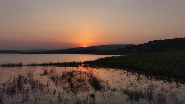 Cinematic aerial drone flight moving forward low over calm lake water towards a golden sunset.