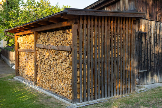 Neatly stacked firewood stored under wooden shelter beside traditional countryside building