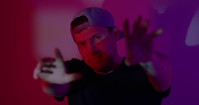 Man wearing cap making hand gesture against neon pink light background. Portrait of guy with serious expression. Modern urban style, trendy fashion lighting and creative visual concept.