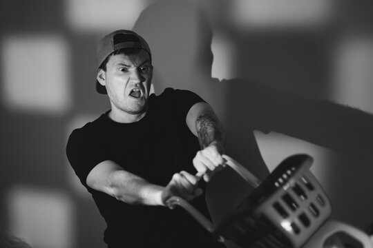 Angry man pushing shopping basket. Aggressive shopper yelling while shopping in store. Consumer behavior and retail frustration. Concept of shopaholic and impulsive buyer in black and white.