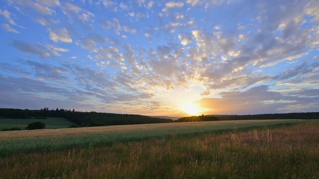 Der Sonnenuntergang taucht den Himmel &uuml;ber einem weiten Feld in warme Oranget&ouml;ne, Wolken ziehen sanft vorbei, Sommer, Gro&szlig;heubach, Miltenberg, Spessart, Bayern, Deutschland