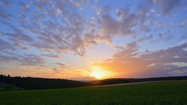 Der Sonnenuntergang taucht den Himmel &uuml;ber einem weiten Feld in warme Oranget&ouml;ne, Wolken ziehen sanft vorbei, Sommer, Gro&szlig;heubach, Miltenberg, Spessart, Bayern, Deutschland