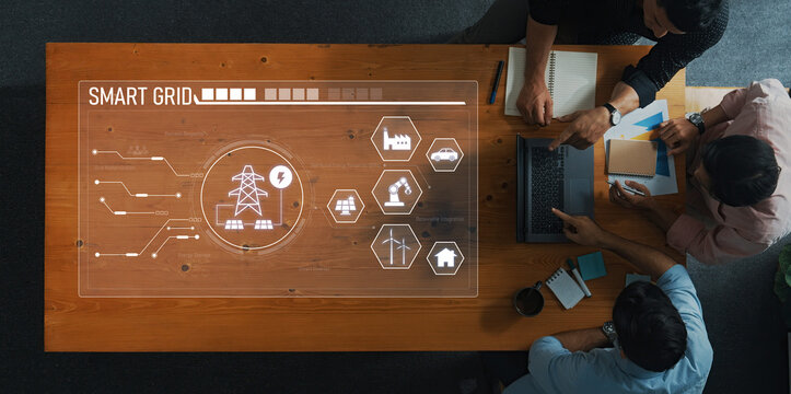 A high-angle view of a team discussing smart grid technology around a table with a digital interface showcasing energy management solutions and data flow visuals. Trope