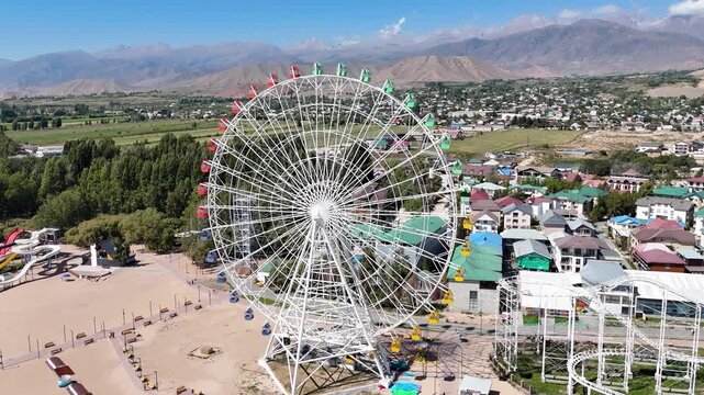 Ferris wheel by Issyk-Kul Lake with scenic mountains in the background, a popular tourist spot.