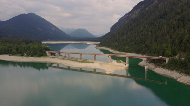 Aerial view of bridge crossing alpine lake with mountain reflections in Plansee, Tyrol, Austria