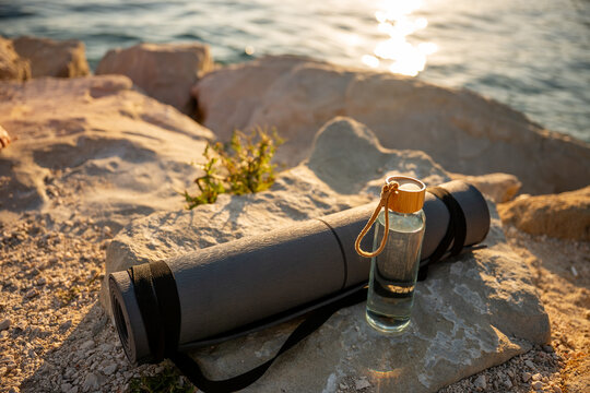 Yoga mat and water bottle on seaside rocks at sunset