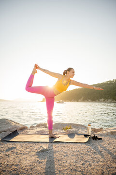 Woman practicing yoga by the sea at sunrise for balance