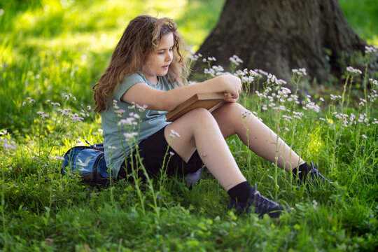 Kid studying outdoors feels calm and peaceful. Smart kid enjoys storytelling in nature. Focused educational kid reads vintage book. Kid portrait shows thoughtful expression.