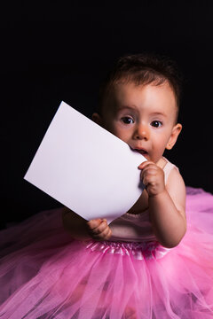 Cute baby girl chewing blank paper with curiosity