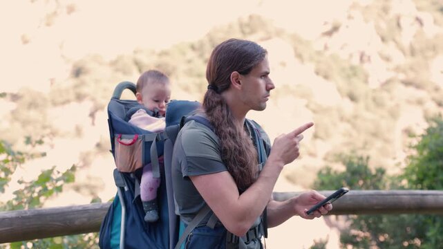 Hiker father using smartphone for navigation with baby in carrier