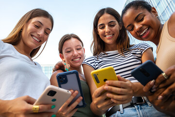 Obraz premium Young women friends laughing using smartphones outdoors