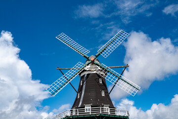 Fototapeta premium Traditional Dutch Windmill under Blue Sky with White Clouds. Classic windmill. Historic rural landmark with wooden retro windmill. Wind power for windmill.
