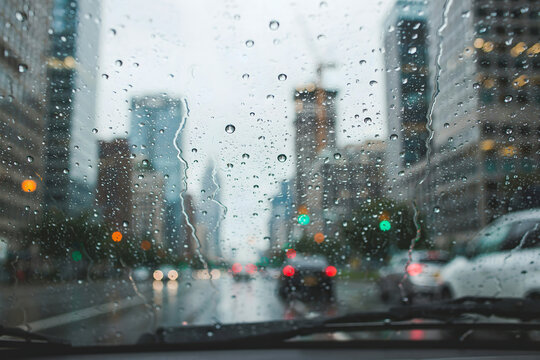 Raindrops on a car windshield with a blurred city street view in the background, showing urban buildings and traffic lights during a rainy day