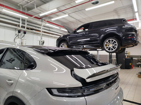 Moscow, Russia - July 25, 2026: Porsche Cayenne cars in the repair area of a car service center. One of the cars is on a lift. Maintenance and repairs are being performed. Selected focus.