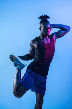 African man perform quad stretch in neon studio light