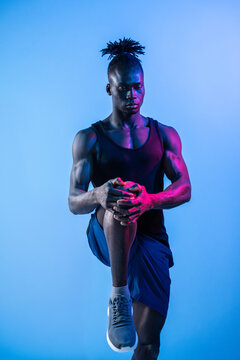 African man performing knee stretch under neon light